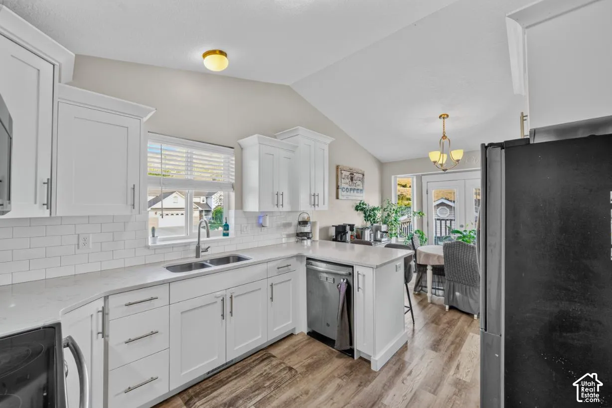 White cabinetry with modern hardware, subway tile backsplash, stainless steel sink, wood-finish flooring, and vaulted ceiling