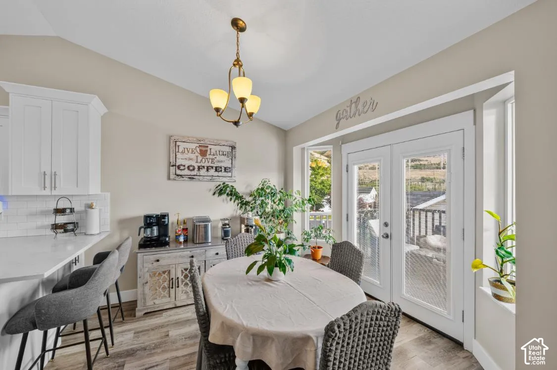 Vaulted ceiling with an overhead chandelier, white shaker-style cabinetry, white subway tile backsplash, wood-finish flooring, and double glass-paneled doors