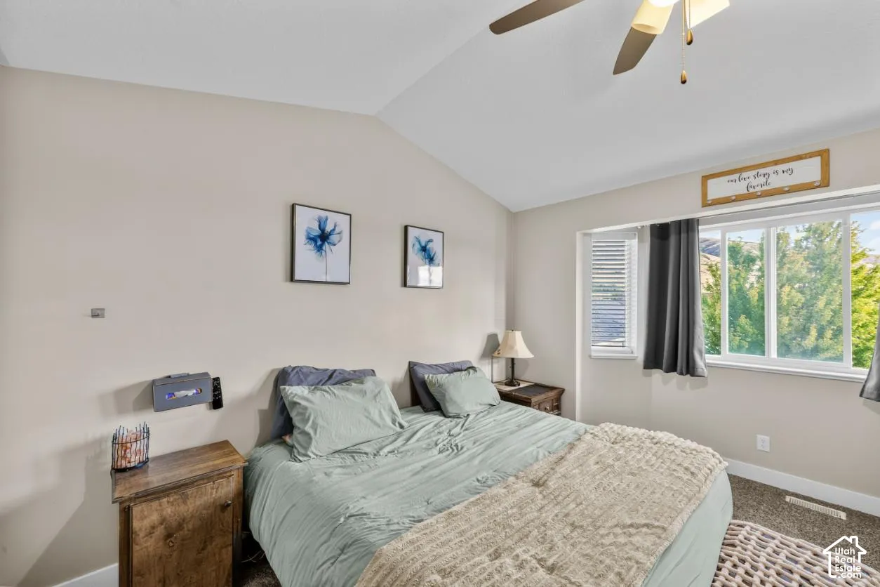 Vaulted ceiling with a ceiling fan, carpeted flooring, and a large window
