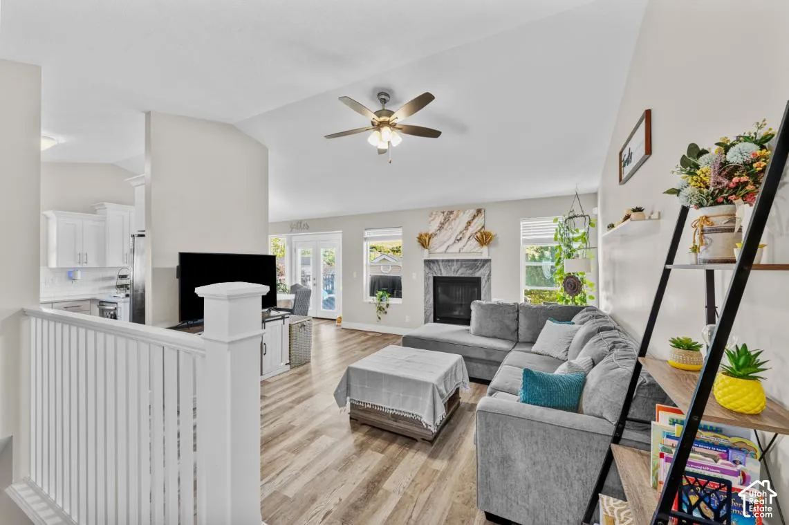 Vaulted ceiling with a ceiling fan, fireplace with a stone surround, wood-finish flooring, white railing, and white kitchen cabinetry