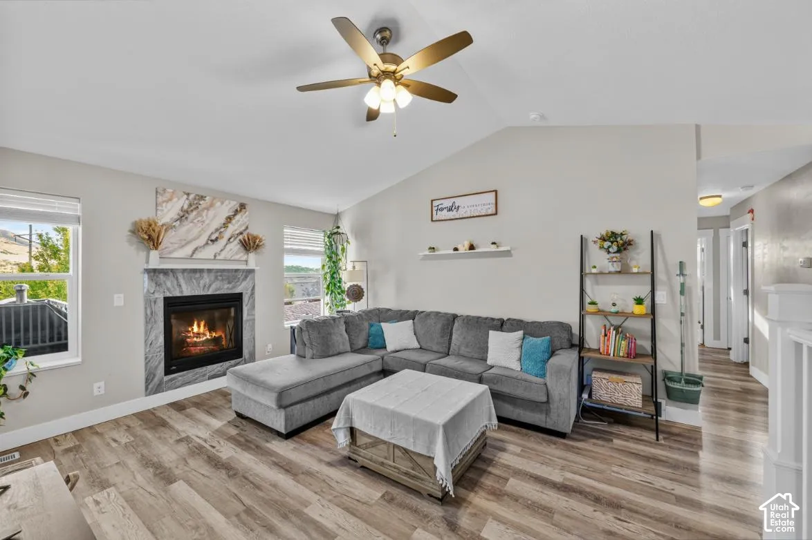 Vaulted ceiling, wood-finish flooring, recessed fireplace with stone surround, ceiling fan, and multiple windows
