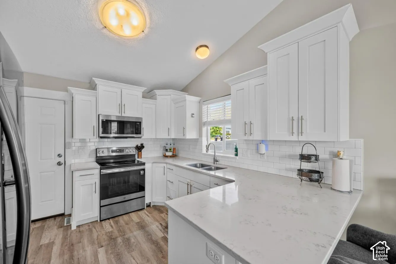White shaker cabinetry, stainless steel appliances, solid surface countertops, subway tile backsplash, and wood-finish flooring