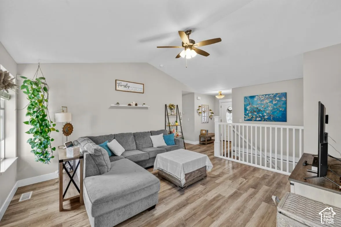 Vaulted ceiling with ceiling fan, wood-finish flooring, white painted railing, and recessed wall shelf