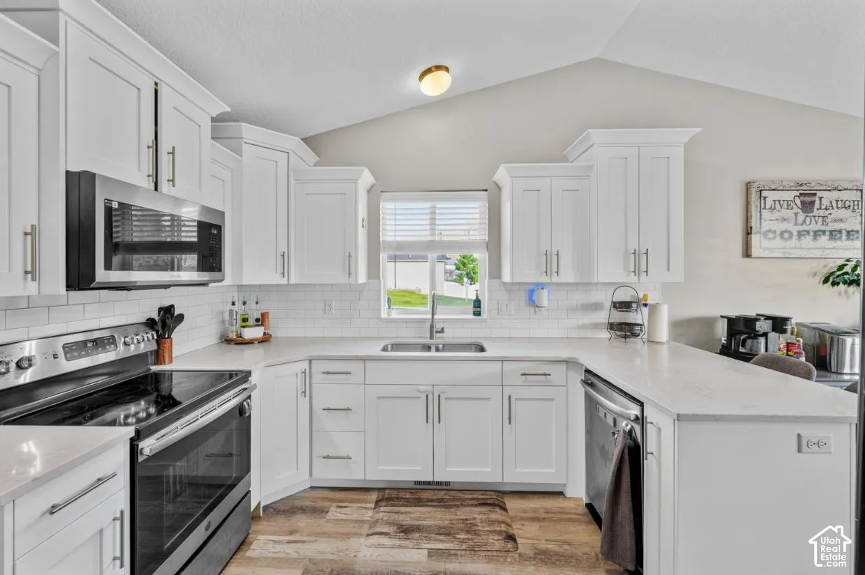 Kitchen featuring white cabinetry, stainless steel appliances, white subway tile backsplash, light-toned countertops, and wood-finish flooring