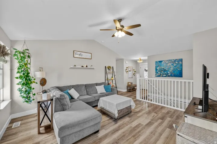 Vaulted ceiling with ceiling fan, wood-finish flooring, white painted railing, and recessed wall shelf