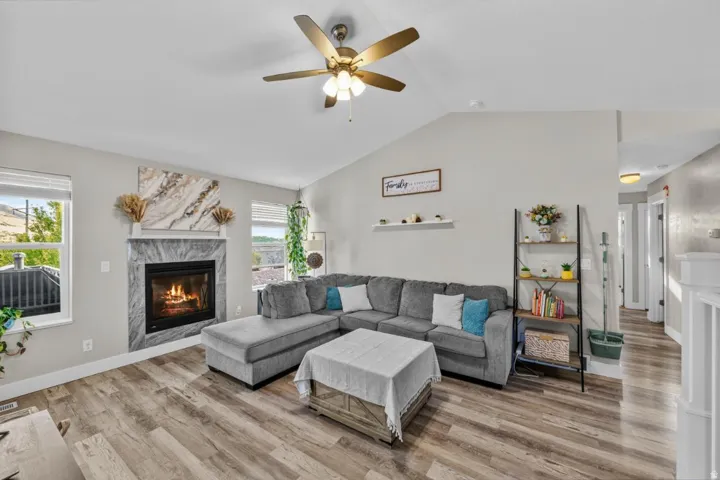 Vaulted ceiling, wood-finish flooring, recessed fireplace with stone surround, ceiling fan, and multiple windows