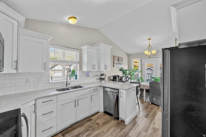 White cabinetry with modern hardware, subway tile backsplash, stainless steel sink, wood-finish flooring, and vaulted ceiling