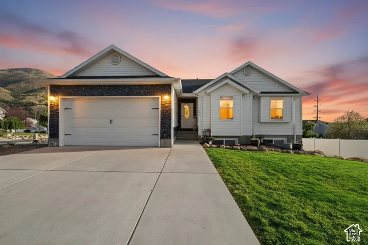 Single-story residence featuring light-colored horizontal siding, stone veneer accents, a paved concrete driveway, an attached two-car garage, and a mountainous backdrop