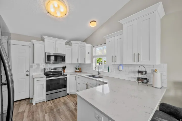 White shaker cabinetry, stainless steel appliances, solid surface countertops, subway tile backsplash, and wood-finish flooring