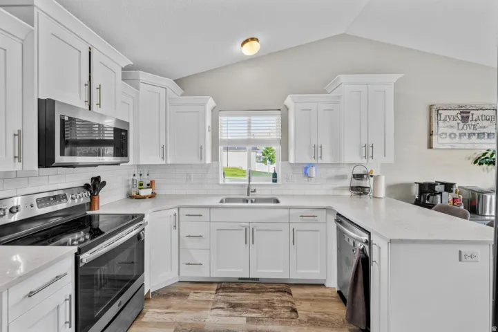 Kitchen featuring white cabinetry, stainless steel appliances, white subway tile backsplash, light-toned countertops, and wood-finish flooring