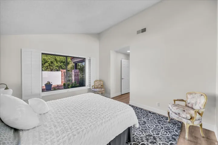 Vaulted ceiling, window with white plantation shutters, wood-finish flooring, white painted walls, and white interior door