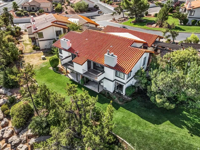 Terracotta tile roof with multiple chimneys, white exterior with dark trim, two balconies, and a sloped lawn