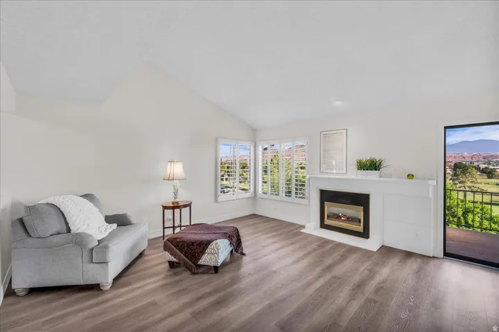 Vaulted ceilings, wood-finish flooring, a fireplace with a white mantel, multiple windows with shutters, and a sliding glass door to exterior