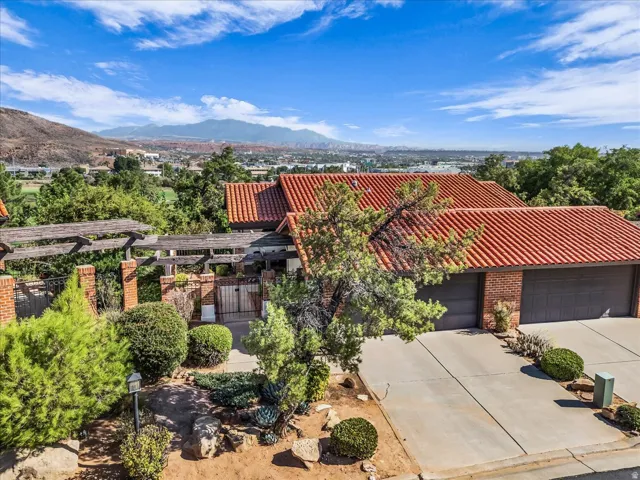 Terracotta tile roofing, brick exterior accents, attached two-car garage, mature landscaping, and mountain scenery
