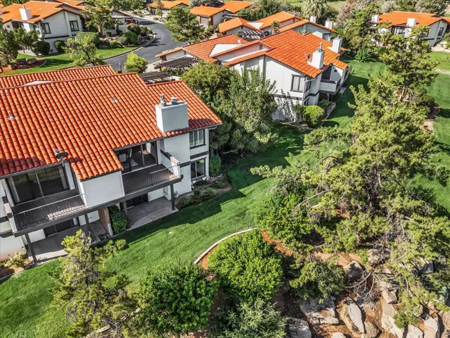 Terracotta tile roofing, balconies with dark railings, stucco exterior, multiple chimneys, and surrounding green landscaping