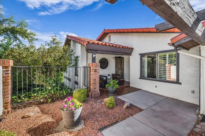 Stucco exterior with a tiled roof, featuring a covered entry, a window with plantation shutters, and a patio with concrete paving and decorative gravel