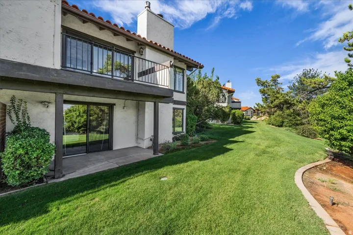 Stucco exterior featuring a second-story balcony with iron railing, ground-level patio, and sliding glass doors