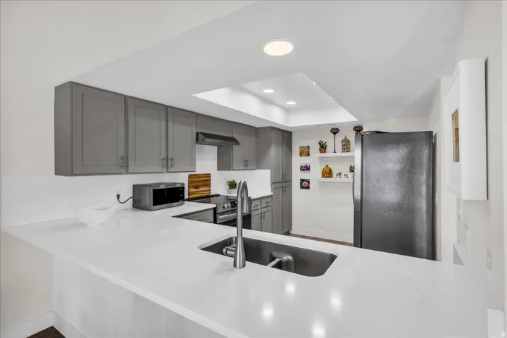 U-shaped kitchen with gray shaker cabinetry, white countertops, stainless steel sink with a gooseneck faucet, and integrated recessed lighting