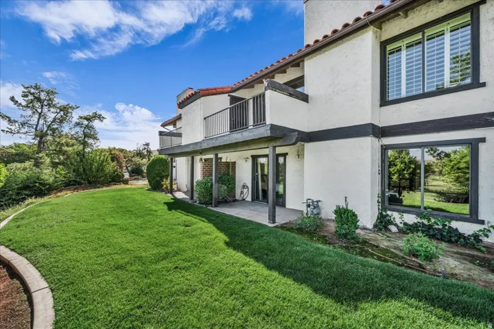 Terracotta tile roof, stucco exterior, upper balcony with dark railings, lower covered patio, and expansive lawn
