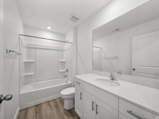 Bathroom featuring a spacious vanity with white cabinetry, a large mirror, a white bathtub with shower, and wood-finish flooring