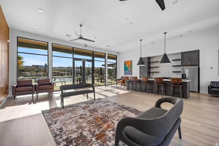 Expansive room with wood-finish flooring, full-height windows, a built-in kitchen area with open shelving, and pendant lighting