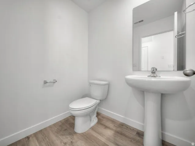 Pedestal sink with chrome faucet, wall-mounted mirror, white toilet, and wood-finish flooring