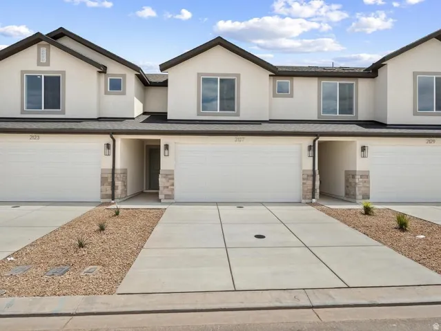 Stucco exterior with stone accents, attached garage, and concrete driveway