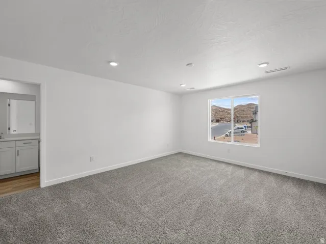 Spacious room featuring neutral carpeting, a large window, recessed lighting, and an adjacent vanity with a mirror
