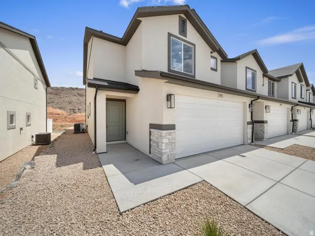 Contemporary stucco exterior with stone accents, integrated garage, concrete driveway, and gravel landscaping