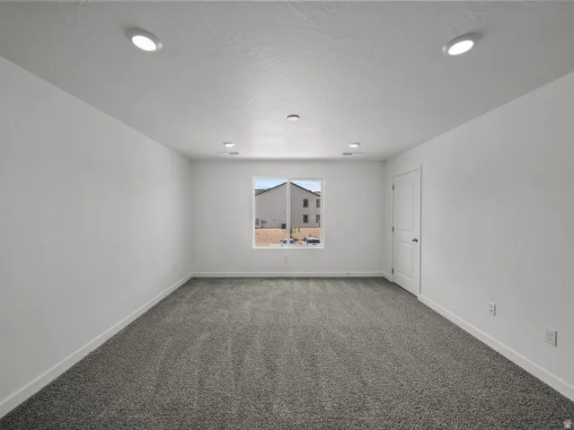 Neutral wall color with gray carpeting, recessed ceiling lighting, and a single window