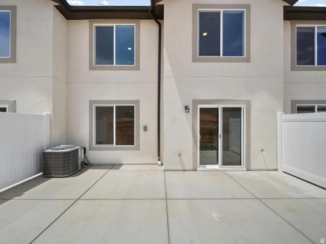 Concrete patio with white privacy fencing, a sliding glass door, and exterior sconce lighting