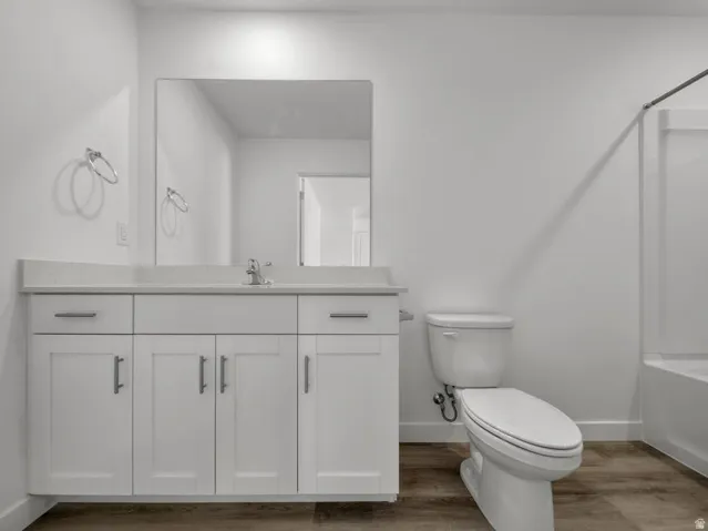 White vanity with integrated sink, rectangular mirror, wood-finish flooring, and a shower-tub combination