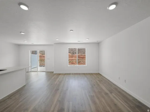 Recessed lighting, wood-finish flooring, white walls, sliding glass door, and a kitchen island with a light-colored countertop