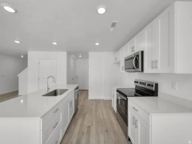 Kitchen featuring white cabinetry, light-toned countertops, wood-finish flooring, stainless steel appliances, and recessed lighting