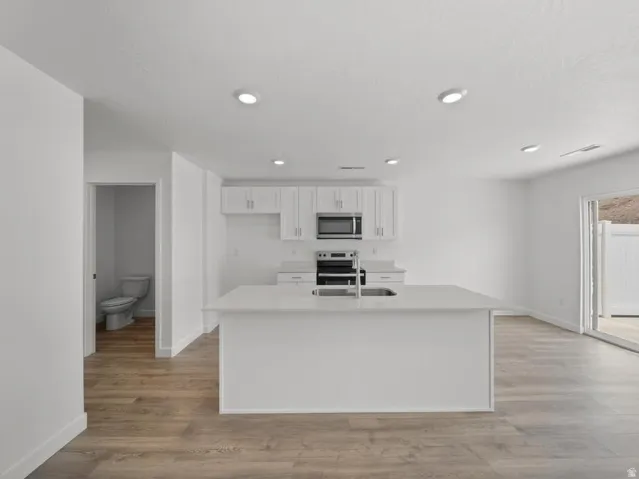 Kitchen with stainless steel appliances, white cabinetry, and a quartz-finish island