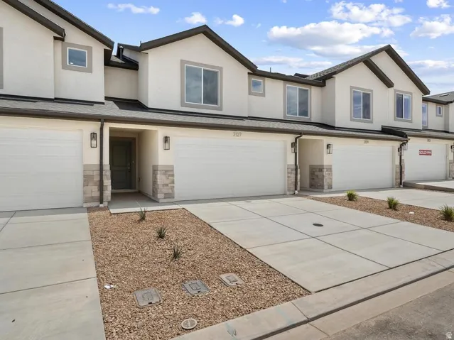 Contemporary townhome exterior featuring an attached garage, a neutral stucco finish, and stone accents