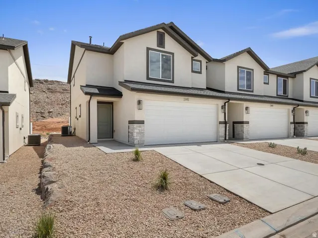 Contemporary stucco exterior with dark trim accents, attached two-car garage, stone veneer detailing, covered entry, and xeriscape landscaping