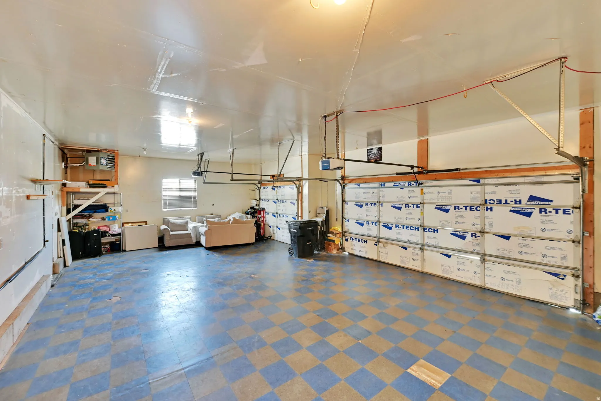 Spacious garage featuring two overhead doors, checkerboard flooring, built-in shelving, and a window for natural light