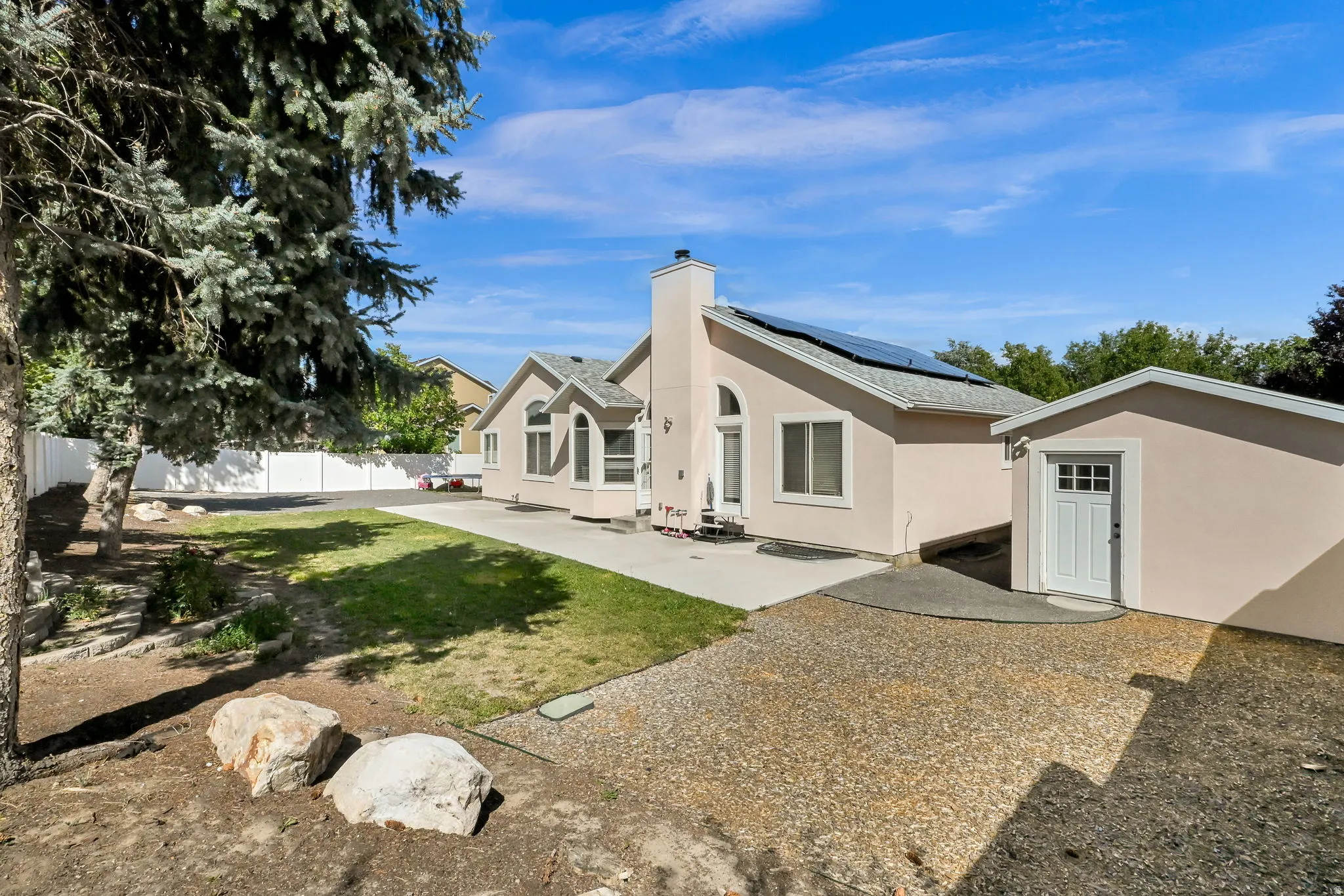 Stucco exterior with multiple windows, solar panels, dedicated outbuilding, and a concrete patio