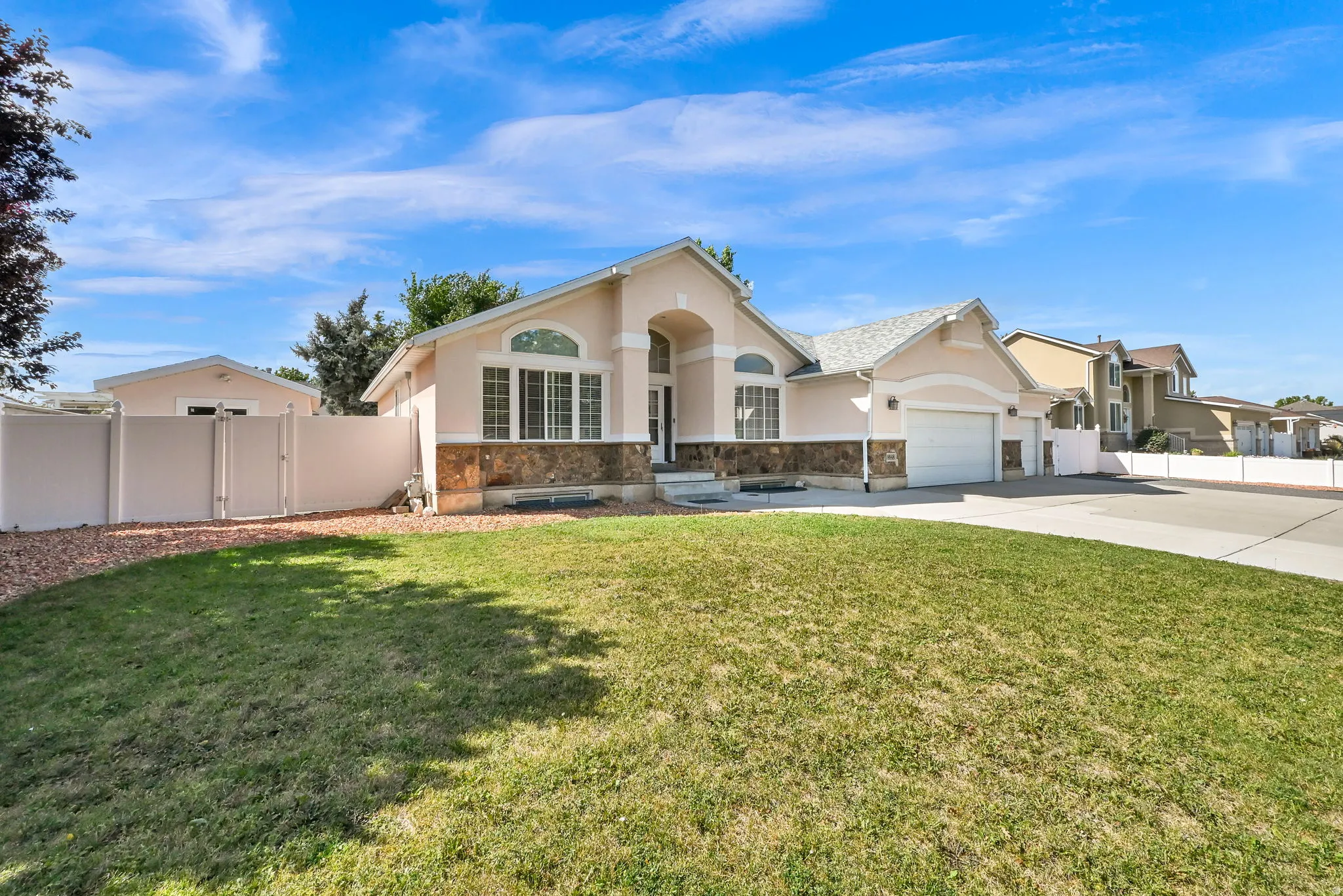 Single-story residence featuring a stucco exterior with stone accents, an attached garage, a front lawn, and a light-colored privacy fence