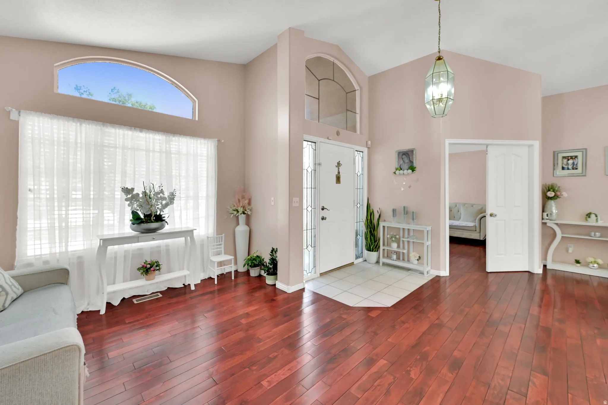 Vaulted ceilings, wood-finish flooring, arched transom window, leaded glass entry door, and a decorative pendant light fixture