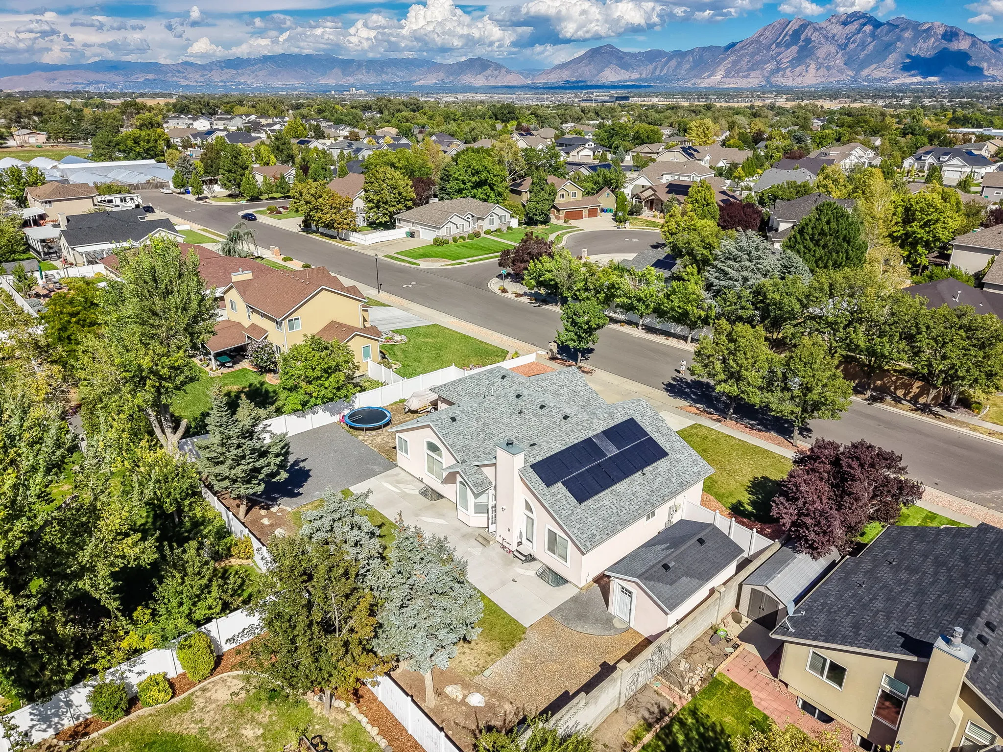 Residential property with solar panels, an asphalt shingle roof, paved driveway, and detached storage structures