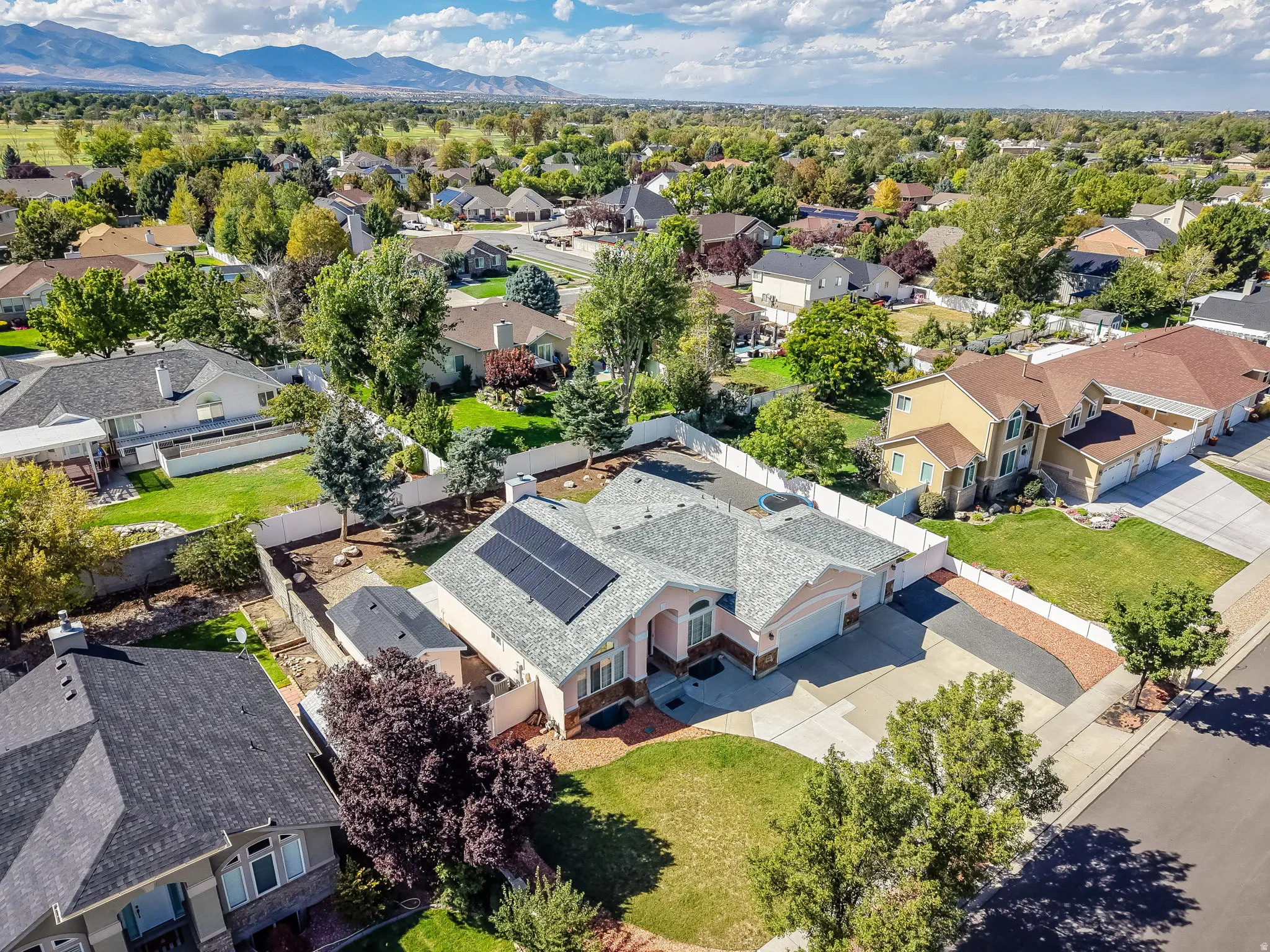 Single-story residence featuring solar panels, an attached two-car garage, a paved driveway, and a white perimeter fence
