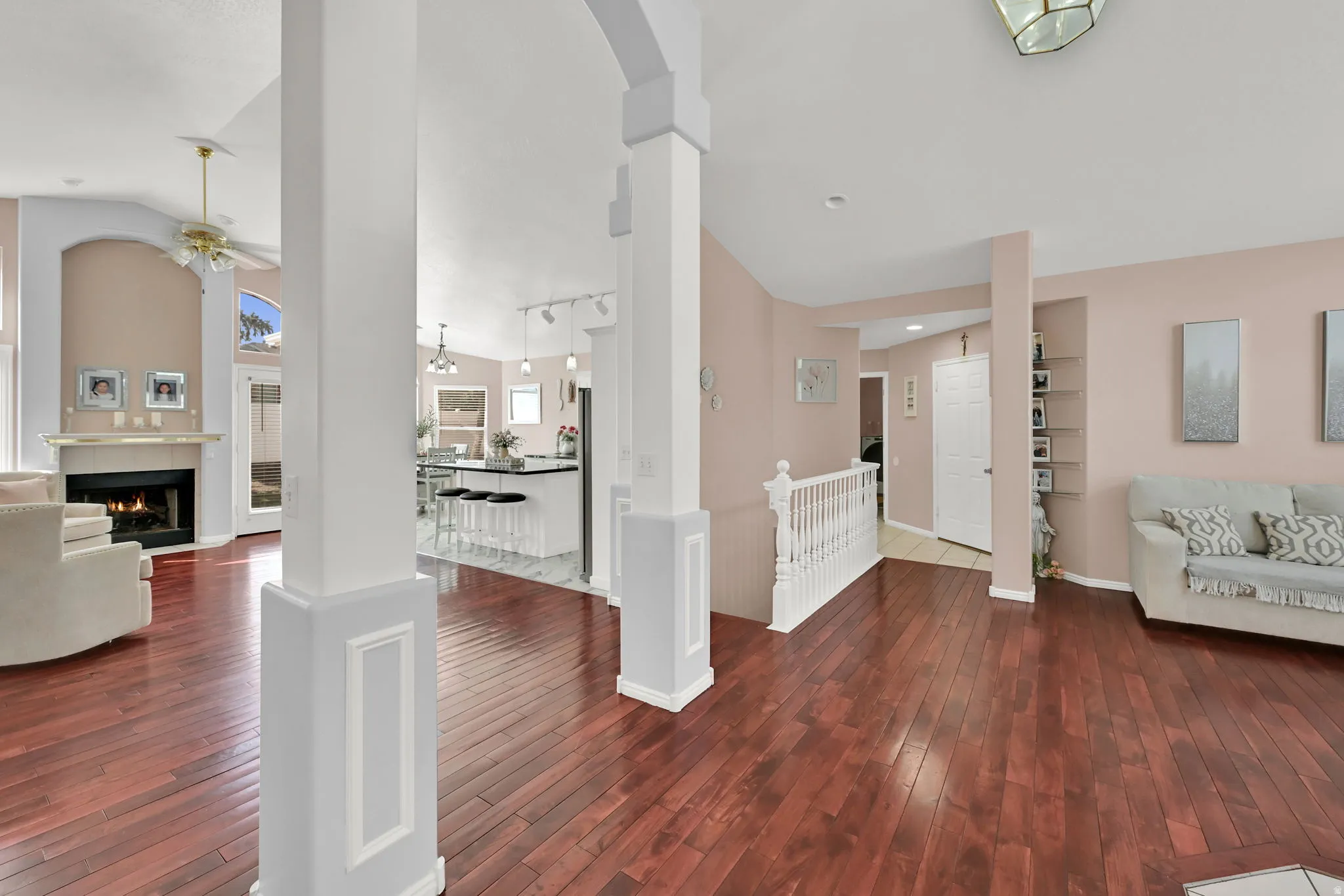 Hardwood flooring throughout, a fireplace with a mantel, white kitchen island with counter seating, white banister, and vaulted ceilings