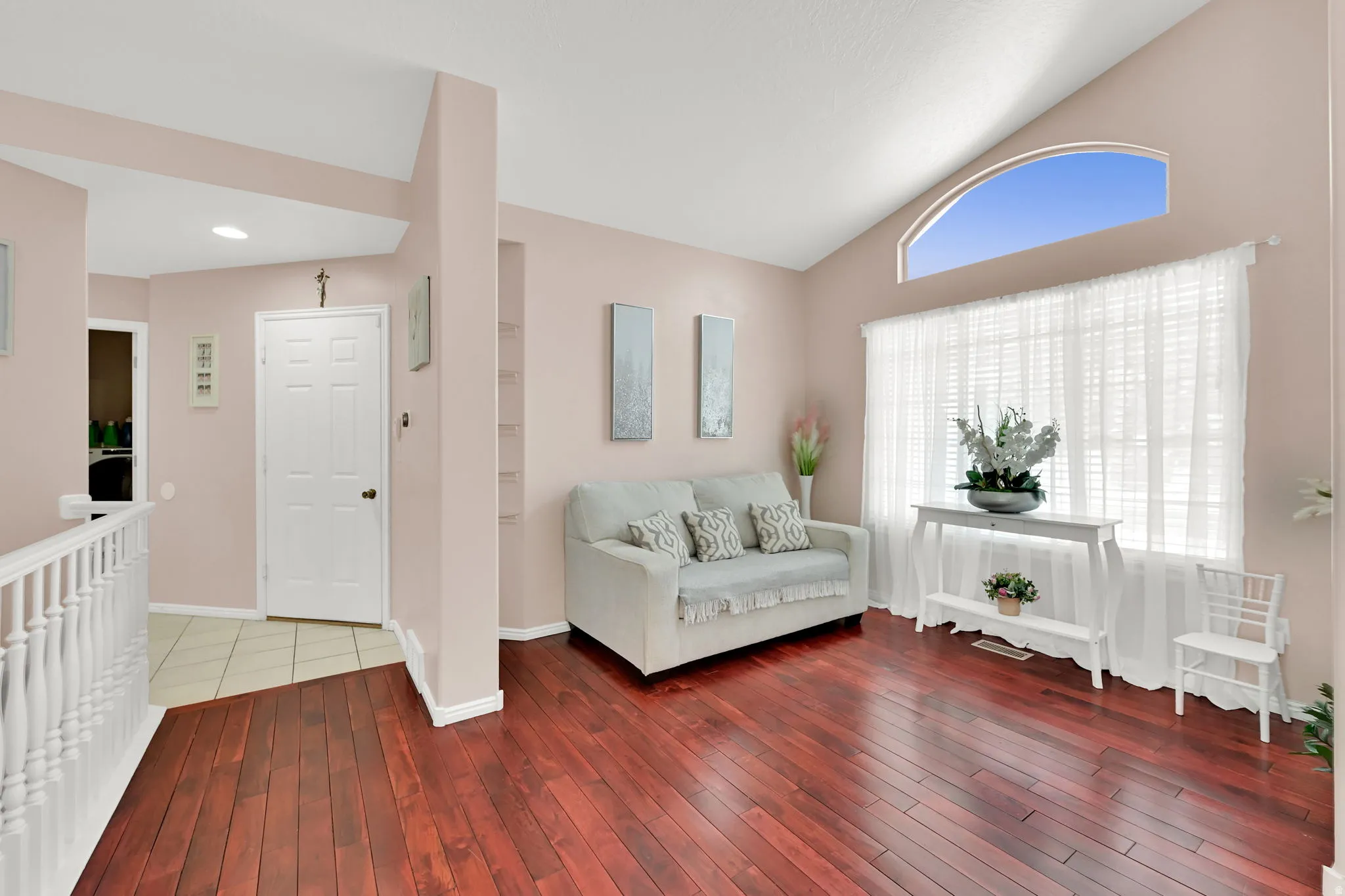 Vaulted ceiling with an arched transom window, wood-finish flooring, and white spindle railing