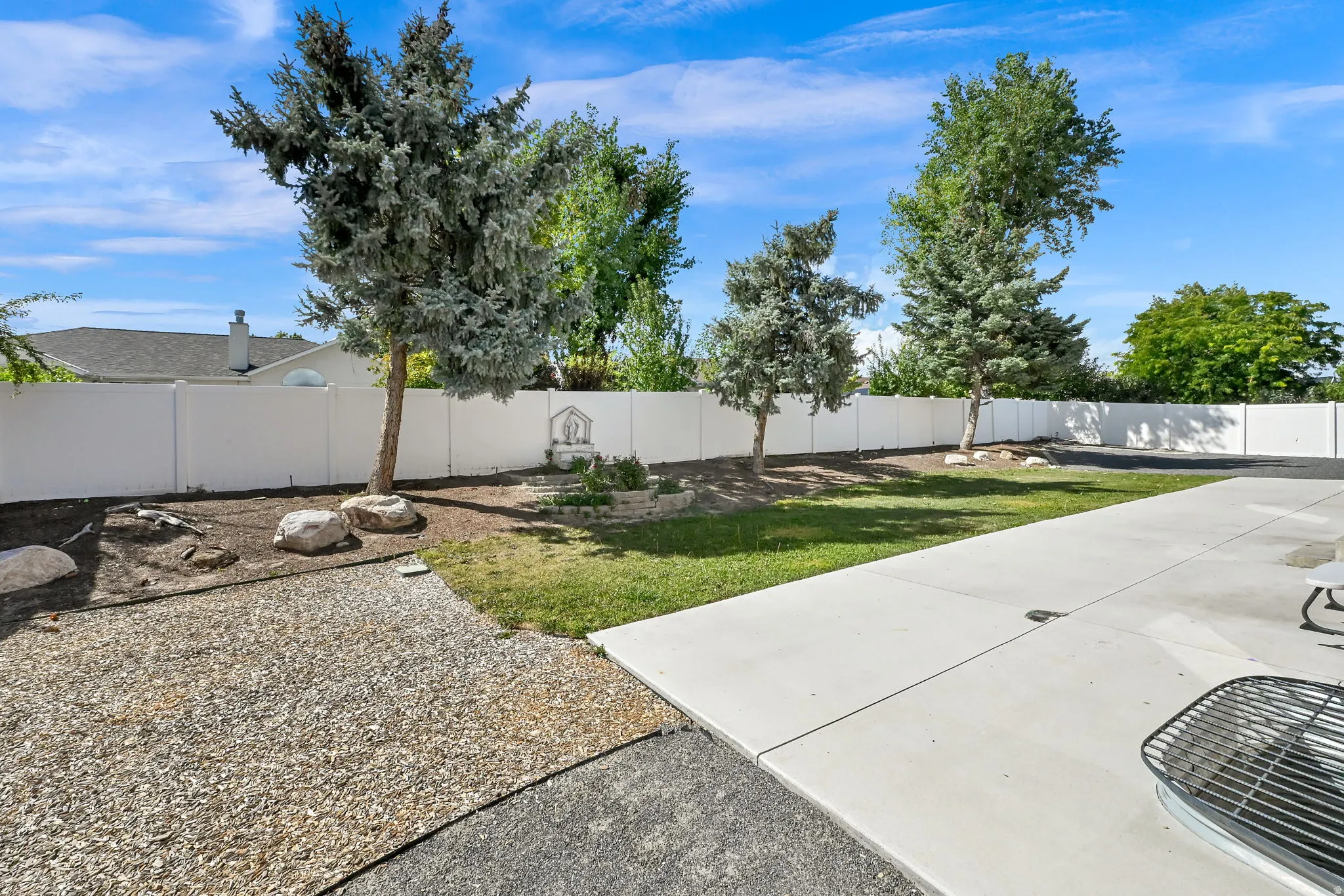 Manicured lawn with mature trees, a white perimeter fence, and a spacious concrete patio