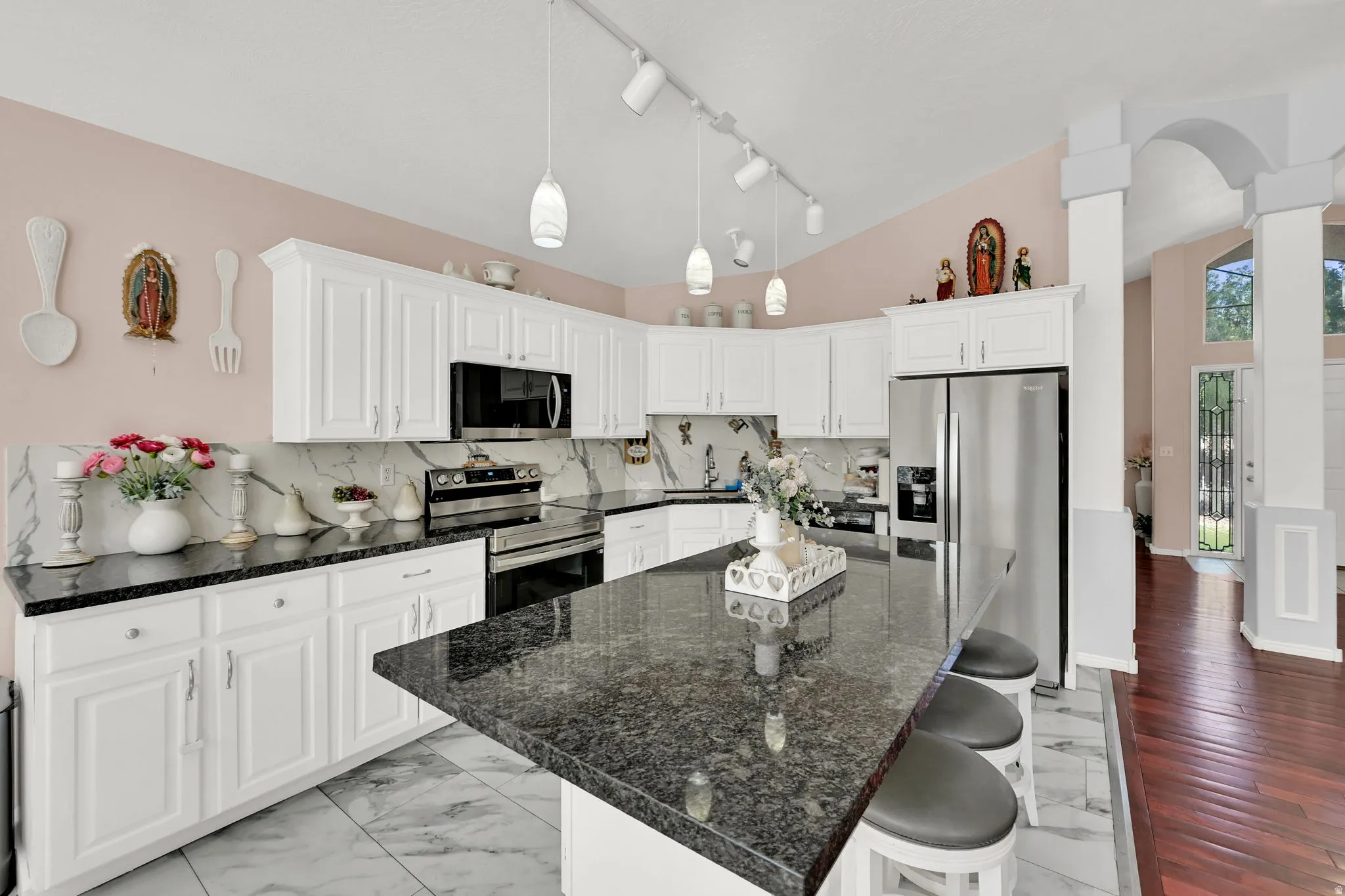 Galley kitchen with white cabinetry, black stone countertops, stainless steel appliances, and track lighting with pendant fixtures