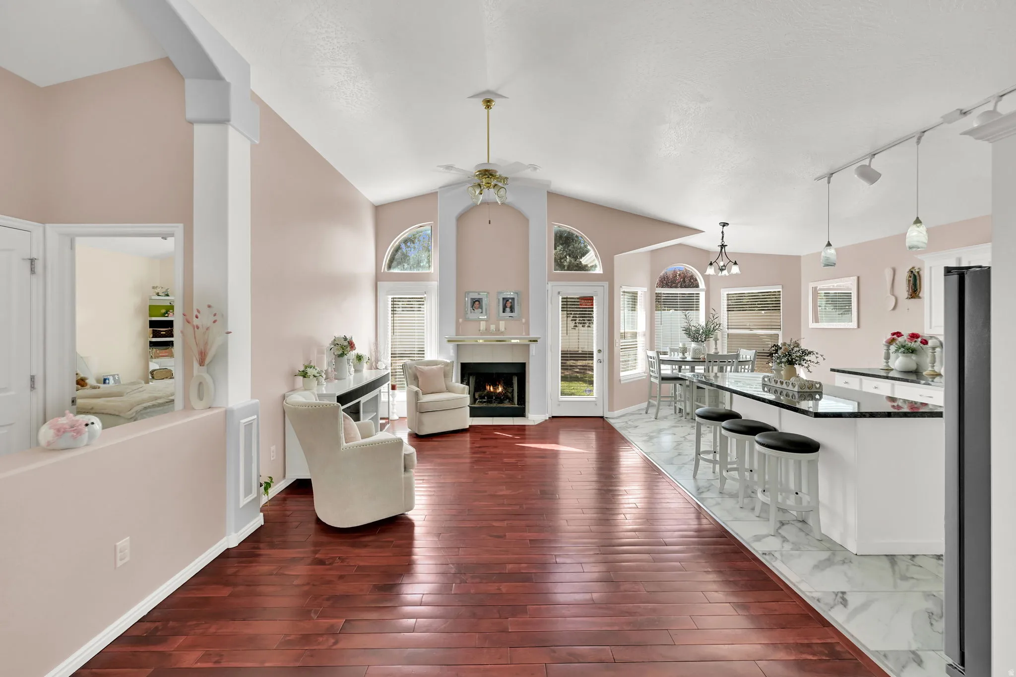 Vaulted ceilings, wood-finish flooring, a fireplace with a mantel, an eat-at kitchen island with a dark countertop, and a dining area with multiple windows