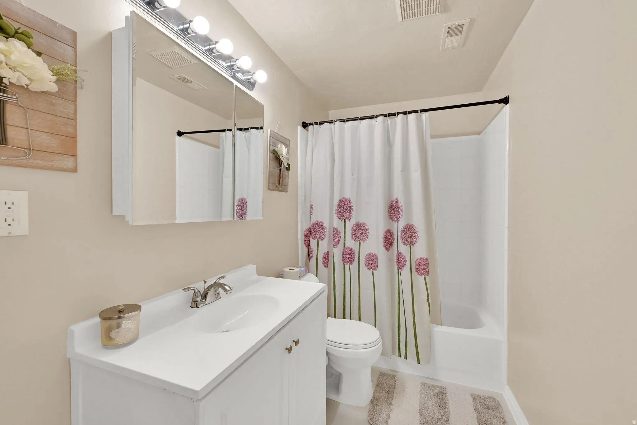 White vanity with integrated sink, chrome faucet, wall-mounted mirrored medicine cabinet with vanity lighting, and a white tub with shower surround