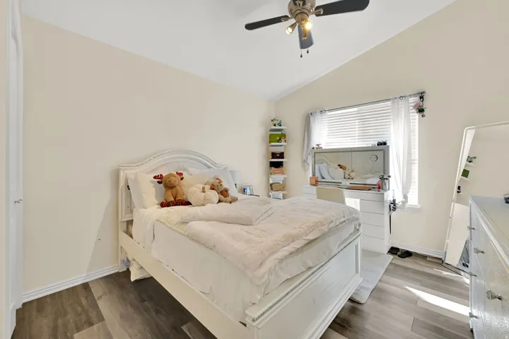 Vaulted ceiling, wood-finish flooring, ceiling fan with integrated lighting, window with blinds, and white trim